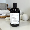 Bottle of Coco Cashmere laundry detergent on a surface with laundry items in the background