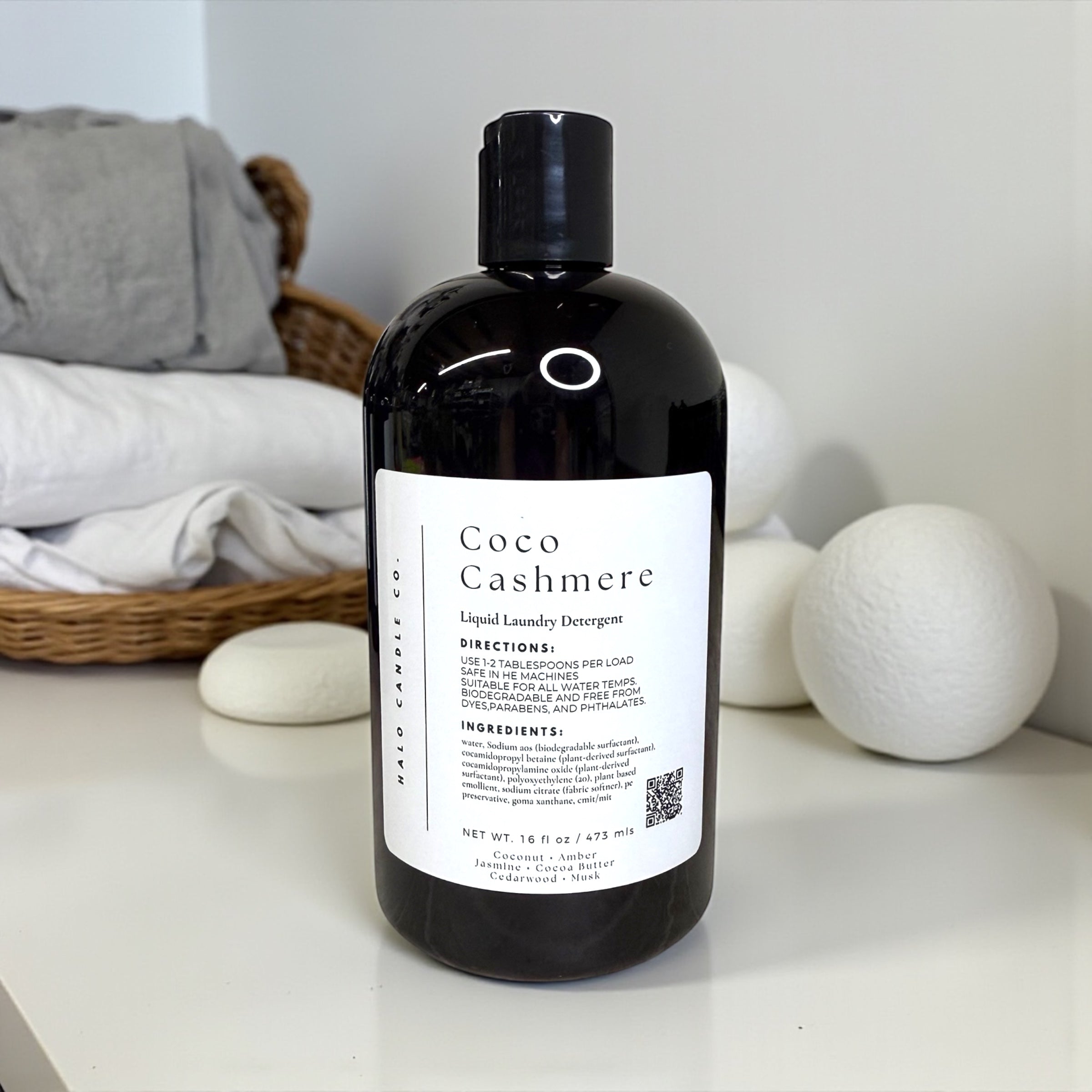 Bottle of Coco Cashmere laundry detergent on a surface with laundry items in the background